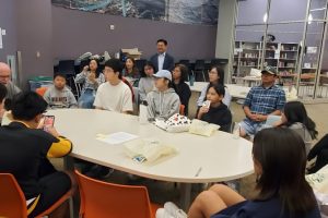 People_gathered_around_a_table_in_a_library People_gathered_around_a_table_in_a_library